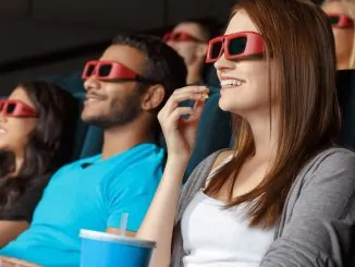 Ein junges Mädchen sitzt im Kino, isst Popcorn und trägt eine 3D Brille