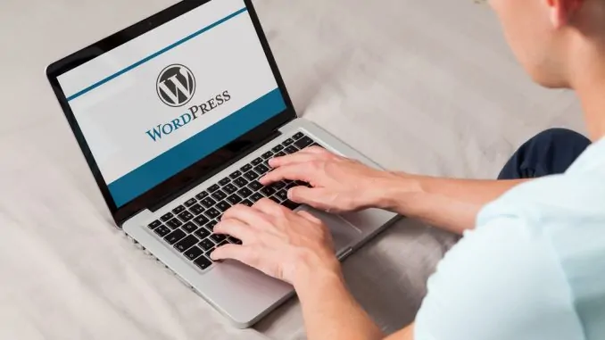 Ein junger Mann sitzt vor dem Laptop auf dem der Schriftzug Wordpress zu sehen ist