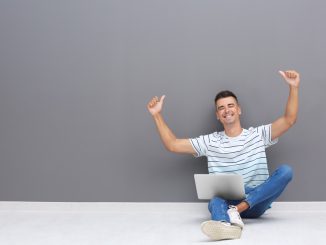 Ein junger Mann sitzt mit dem Notebook auf dem Boden und schreibt eine Kurzbewerbung