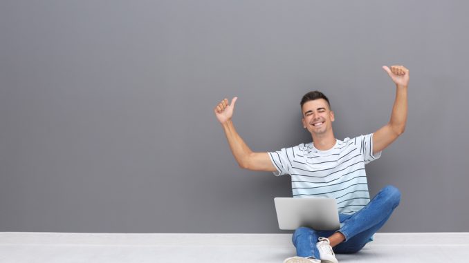 Ein junger Mann sitzt mit dem Notebook auf dem Boden und schreibt eine Kurzbewerbung