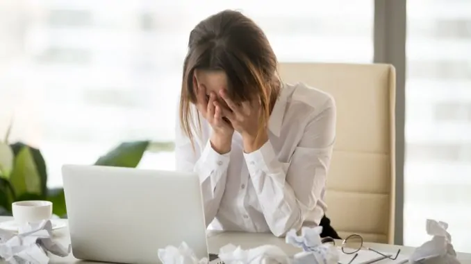 Eine junge Frau sitzt hilflos am Arbeitsplatz vor dem Notebook