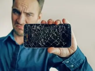 Ein junger Mann hält ein Smartphone mit Displayschaden in die Kamera