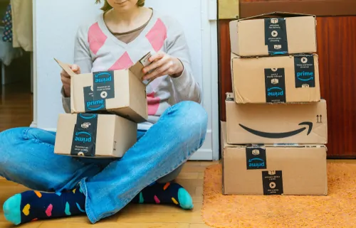 Ein junges Mädchen sitzt auf dem Boden. Um sie herum stehen Amazon Prime Pakete