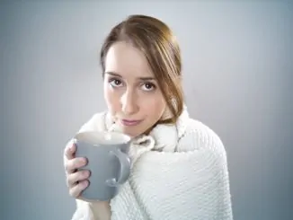 Ein junges Mädchen mit Schal um den Hals und einer blauen Tasse in der Hand