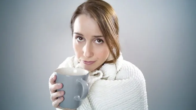 Ein junges Mädchen mit Schal um den Hals und einer blauen Tasse in der Hand