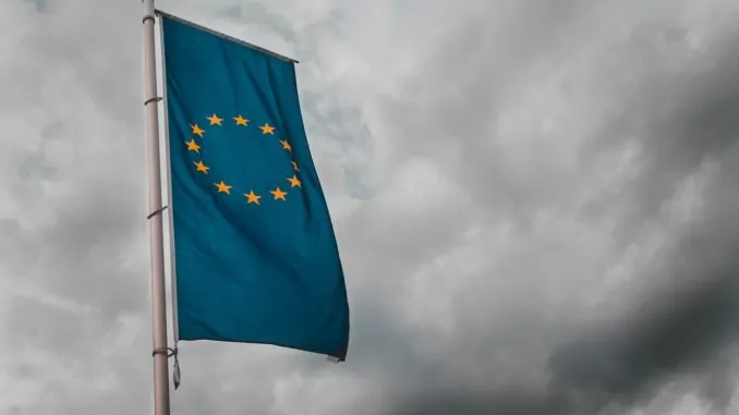 Eine blaue gelbe Fahne der europäischen Union weht im Wind vor dunklen Wolken