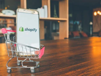 Handy mit Shopify-App auf dem Bildschirm im Einkaufswagen auf Holztisch.