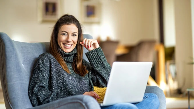 Eine junge Dame mit braunen Haaren sitzt mit einem weißen Notebook auf einem blauen Sessel.