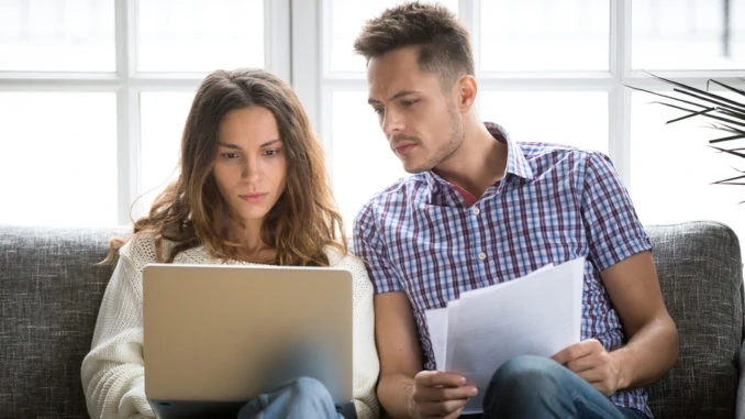 Eine junge Frau und ein junger Mann sitzen auf der Couch und schauen auf ein Notebook