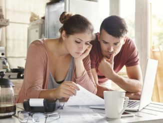 Eine junge Frau und ein junger Mann sitzen vor dem Notebook und führen ein digitales Haushaltsbuch
