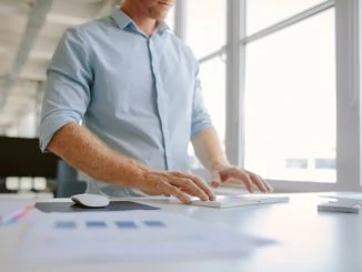 Ein junger Mann in blauem Hemd arbeitet im Stehen am Computer.