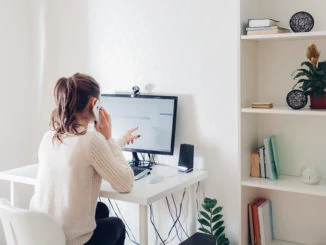 Eine junge Frau sitzt zuhause im Home Office vor dem Computer und arbeitet selbstständig