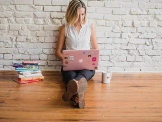 Eine Influencerin sitzt auf dem Boden mit ihrem Notebook auf dem Schoß