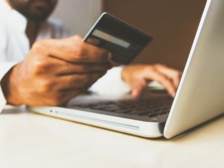 Mann sitzt mit Kreditkarte in der Hand am Laptop