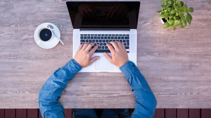 Mann sitzt vor aufgeklappten Laptop